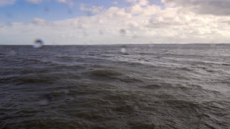 Choppy-sea-under-blue-sky-with-some-cloud,-droplets-of-water-on-lens