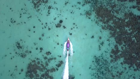 4k-View-from-above,-stunning-aerial-shot-following-long-tail-boat-in-a-turquoise-and-clear-sea,-Phi-Phi-Islands,-Thailand,-surrounding-by-water