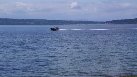 Small,-nondescript-fishing-boat-cruising-past-beach-at-Camano-Island-State-Park,-WA-State