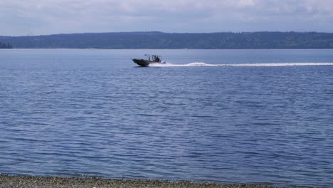 Small,-nondescript-fishing-boat-cruising-past-beach-at-Camano-Island-State-Park,-WA-State