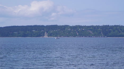 Distant-sailboat-motoring-past-beach-at-Camano-Island-State-Park,-Washington-State-10sec-24fps-slow-motion