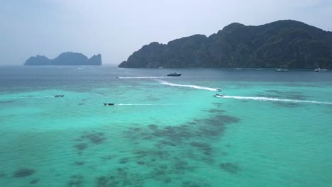 4K-AERIAL-VIEW-of-Long-tail-boats-sailing-in-emerald-sea-in-Phi-Phi-Don's-bay,-Thailand,-boat-traffic,-surrounding-by-limestone-cliff