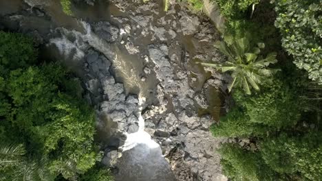 AERIAL-FLYING-OVERHEAD-A-WATERFALL,-Tegenungan,-beautiful-river-course-in-Bali,-Indonesian