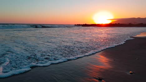 Very-low-gimbal-shot-of-beach-at-sunset-with-waves-crashing-at-San-Buenaventura-State-Beach-in-Ventura,-California,-United-States