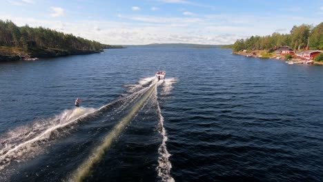 Zeitlupe-Einer-Drohne,-Die-Im-Sommer-über-Einen-Jungen-Mann-Fliegt,-Der-Auf-Einem-Wakeboard-Nach-Einem-Sportboot-In-Den-Schwedischen-Schären-Reitet-Sub3