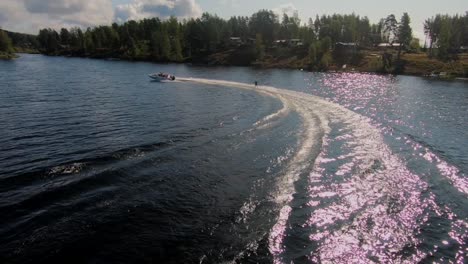 Zeitlupe-Einer-Drohne,-Die-Im-Sommer-über-Einen-Jungen-Mann-Fliegt,-Der-Auf-Einem-Wakeboard-Nach-Einem-Sportboot-In-Den-Schwedischen-Schären-Reitet-Sub4