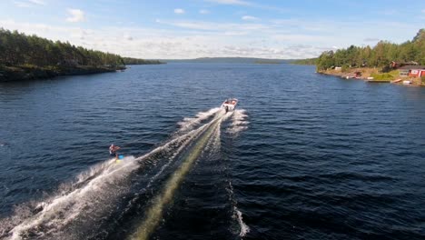 Drohne-Fliegt-über-Einen-Jungen-Mann,-Der-Im-Sommer-Auf-Einem-Wakeboard-Nach-Einem-Sportboot-In-Den-Schwedischen-Schären-Reitet-Sub2