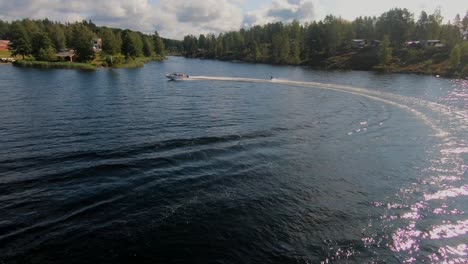 Drohne-Fliegt-über-Einen-Jungen-Mann,-Der-Im-Sommer-Auf-Einem-Wakeboard-Nach-Einem-Sportboot-In-Den-Schwedischen-Schären-Reitet
