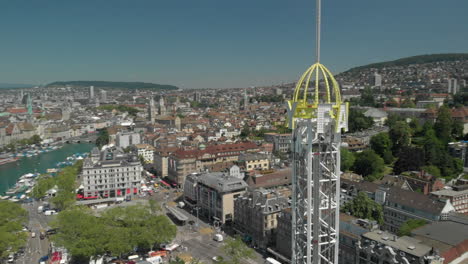 Aerial-drone-shot-orbiting-flyby-around-amusement-park-free-fall-tower-with-the-city-and-lake-of-Zürich,-Switzerland-in-the-background-during-Zürichfest