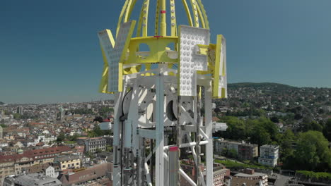 Aerial-drone-shot-orbiting-around-amusement-park-free-fall-tower-and-flying-backwards-revealing-the-city-of-Zürich,-Switzerland-during-Zürichfest