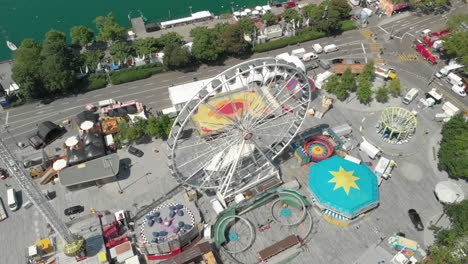 Beautiful-orbiting-aerial-drone-shot-flying-down-and-around-amusement-park-Ferris-wheel-with-the-city-of-Zürich,-Switzerland-in-the-background-during-Zürichfest-60fps