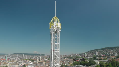 Aerial-drone-crane-shot-rising-up-and-tilting-down-of-amusement-park-Ferris-wheel-and-free-fall-tower-with-the-city-and-lake-of-Zürich,-Switzerland-in-the-background-during-Zürichfest