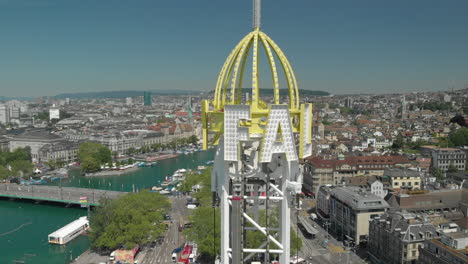 Aerial-drone-shot-orbiting-around-amusement-park-free-fall-tower-and-flying-backwards-revealing-the-city-and-lake-of-Zürich,-Switzerland-during-Zürichfest