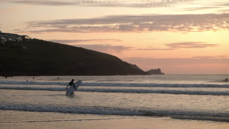 Surfer-walking-into-the-ocean-at-sunset