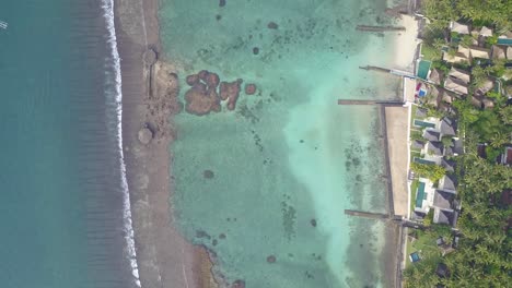 top-view-of-a-clear-water-reef-and-houses-on-the-beach-surrounded-by-palm-trees