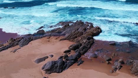 Aerial-shot-of-a-coastline-where-the-ocean-meets-the-shore-with-rocks