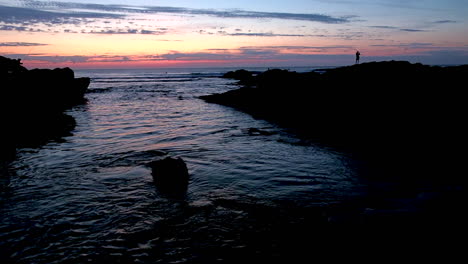 Leute-Auf-Den-Felsen,-Die-Den-Sonnenuntergang-Mit-Blick-Auf-Den-Strand-Beobachten