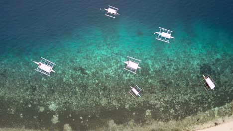 Bay-of-bangka-boats-on-clear-blue-water-in-Philippines,-drone-shot-descending-towards-the-sea