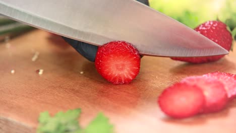 Slicing-fresh-strawberry-on-a-wooden-board-with-a-large-knife-into-slices,-close-up-of-cook-hands-with-black-gloves