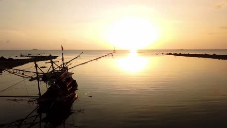 Aerial-view-of-fishing-boat-silhouette-and-sunset-over-skyline-and-calm-sea-water,-Thailand