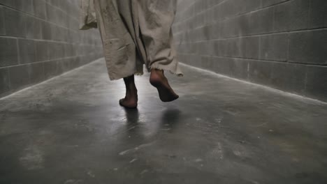 Closeup-of-the-feet-of-Jesus-Wearing-White-Robe-Walks-In-Prison-Hallway-In-Slow-Motion
