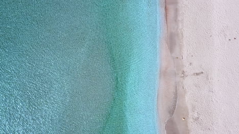 Top-down-aerial-view-of-an-empty-tropical-white-sands-beach-and-water-as-it-ripples-gently-in-the-sun