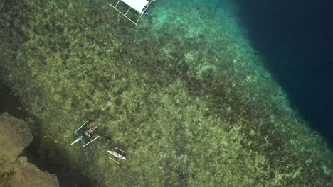 Philippines-village-on-clear-sea-with-fishing-boats-and-coral-reef,-rising-up-drone-shot