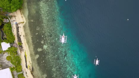 Village-on-clear-water-in-Philippines-with-fishing-boats,-drone-shot-of-a-coral-reef-along-the-coastline