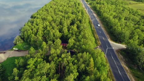 Road-trip-on-empty-highway-aligned-by-green-pine-trees-along-Tornio-river