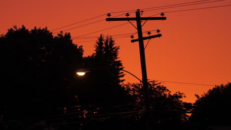 Straßenlaterne-Und-Stromleitungen-Mit-Einem-Orangefarbenen-Himmel-Im-Hintergrund