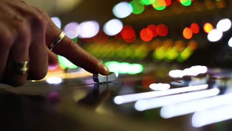 Audio-Technician-moving-gently-by-finger-button-of-TV-Audio-mixer-on-a-live-broadcasting-event,-blurry-colorful-background