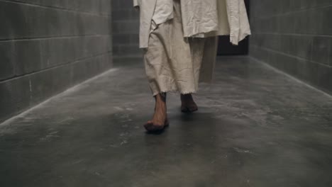 Closeup-of-the-feet-of-Jesus-wearing-white-robe-walking-in-slow,-dramatic-fashion-in-prison-hallway