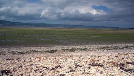 Shell-beach-along-Belfast-lough-with-tide-out-hills-in-background-and-moving-clouds-above