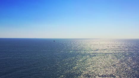 Shimmering-wide-view-of-open-water-and-the-horizon-with-a-single-boat-sailing-in-the-distance