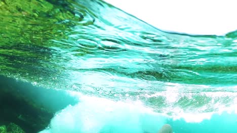 Man-diving-into-emerald-sea-foaming-bubbles-inside-clean-water,-slow-motion