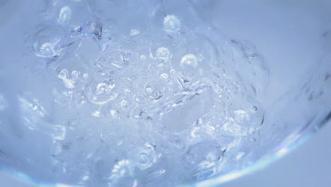 Zeitlupe---Aufnahme-Von-Wasser,-Das-In-Ein-Glas-Mit-Eiswürfeln-Mit-Hellblauem-Und-Weißem-Hintergrund-Gegossen-Wird
