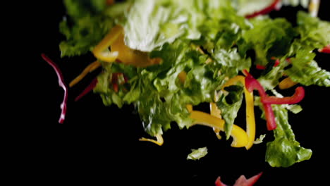 Slow-Motion---Close-shot-of-freshly-cut-salad-flying-through-the-air-in-front-of-a-black-background