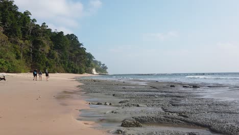 Slow-motion-walking-with-camera-along-the-beach-at-low-tide-in-the-andaman-islands-with-three-people-and-a-dog-in-the-distance-and-forest-lining-the-remote-beach