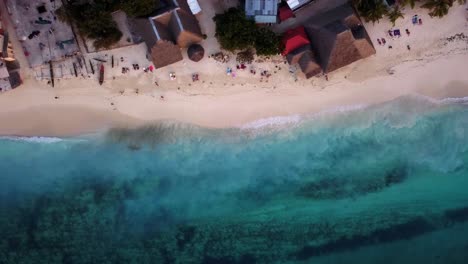 Aerial-Birdseye-shot-of-People-walking-and-Relaxing-on-Nungwi-Beach-as-Small-Waves-Crash-on-the-Sandy-Shore-Zanzibar,-Unguja,-Island-in-Tanzania-during-Sunset