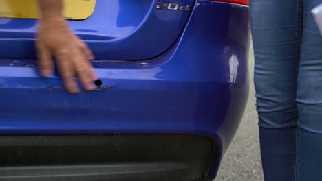 Car-crash-rear-end-bumper-damage-blue-paint-man-shows-woman-driver-the-accident-impact-area