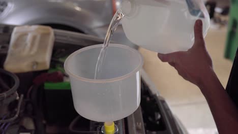 Man-pours-coolant-from-jug-into-radiator-using-large-funnel-in-garage