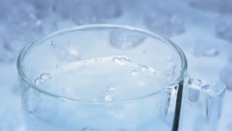 Slow-Motion---Ice-cub-is-dropped-into-a-glass-of-water-creating-a-big-splash-on-a-light-blue-and-white-table-with-ice-cubes