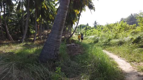 A-man-and-a-woman-walking-along-a-remote-path-past-large-coconut-trees-and-indian-forest