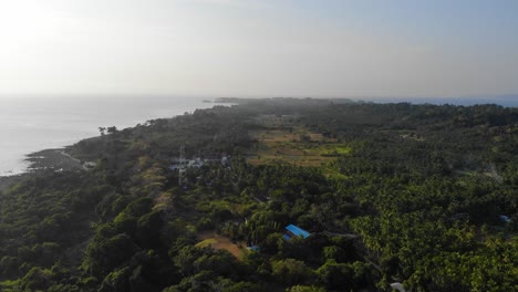 Panoramic-drone-view-of-andaman-island-at-sunset-with-the-andaman-sea-in-the-background-and-farmland-in-the-foreground-with-small-homesteads-,-forest-and-fields-and-radio-tv-internet-tower