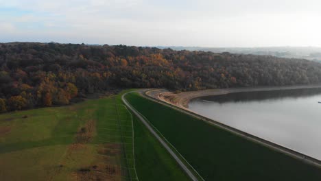Forward-drone-aerial-movement-with-autumn-colours-and-dam-of-reservoir-with-walkway-and-walkers