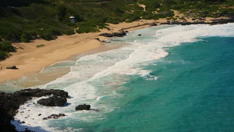 Large-waves-rolling-on-the-east-coast-of-Oahu-in-summer-with-sandy-beach,-black-volcanic-rock-and-some-tourists
