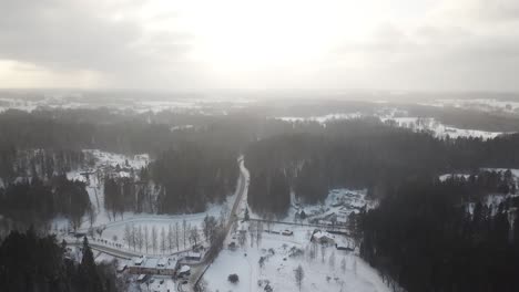 Hoch-über-Einer-Kleinen-Winterstadt-Mit-Sonnenlicht,-Das-Durch-Die-Wolken-Und-Leichtem-Schnee-In-Der-Luft-Dringt