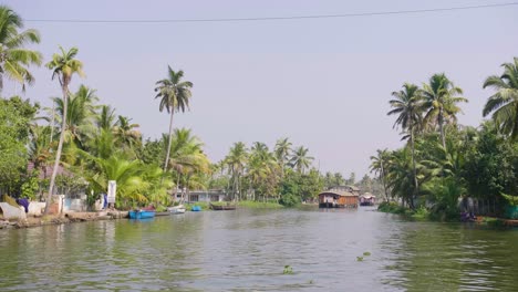 Kerala-backwater-boats-moving-into-the-distance-away-from-the-camera-along-the-canals-in-the-heat-of-the-day-with-palms-both-sides