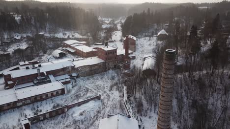 Old,-abandoned-factory-buildings-with-snowy-roof-tops-and-two-tall-chimney-towers-in-Ligatne,-Latvia