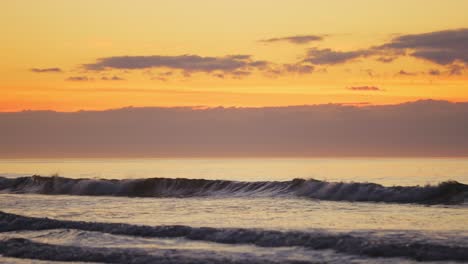 Slow-motion-shot-of-waves-during-beautiful-golden-sunrise-in-background